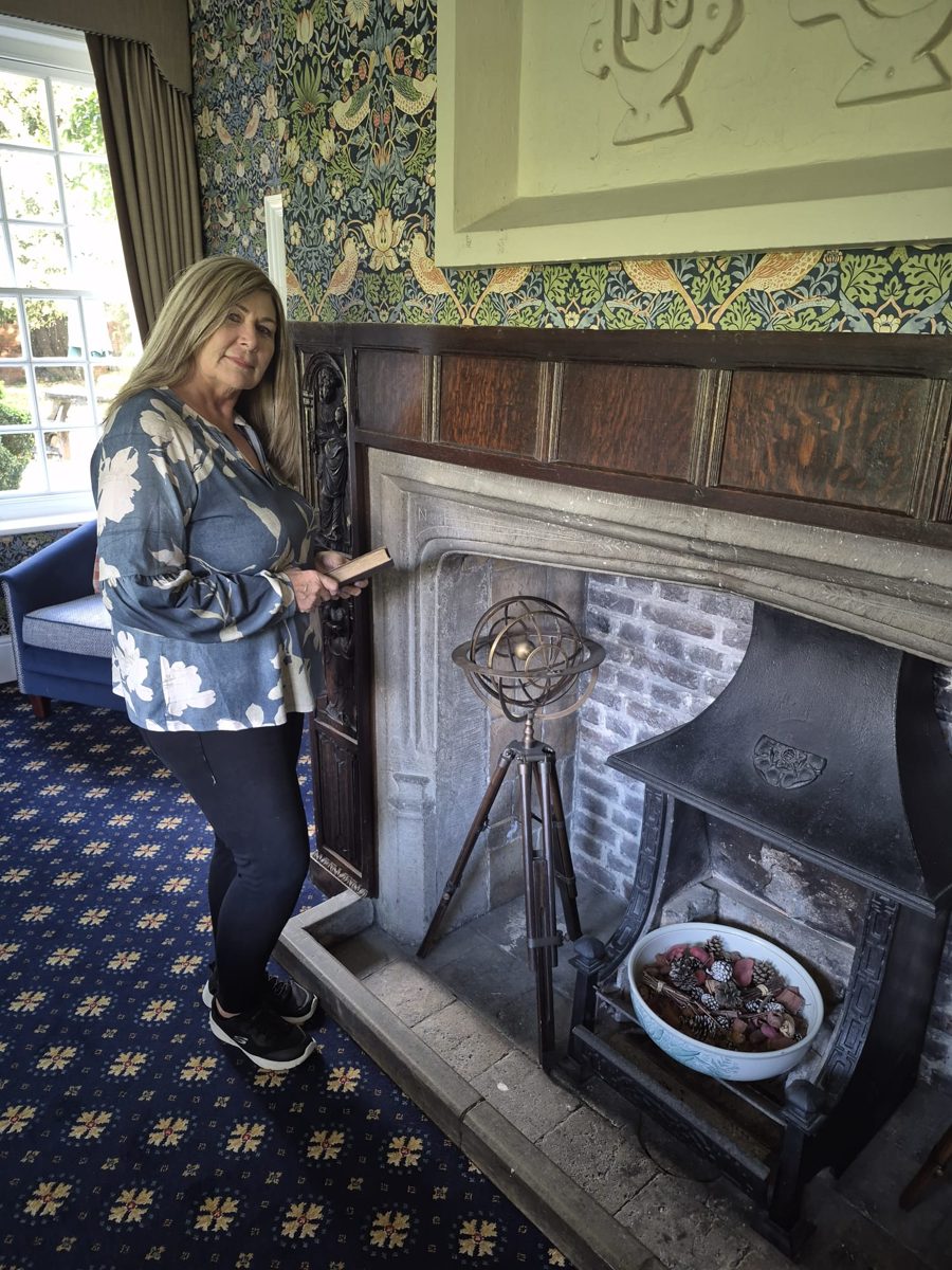 Clare Kiernan standing beside a fireplace holding a book
